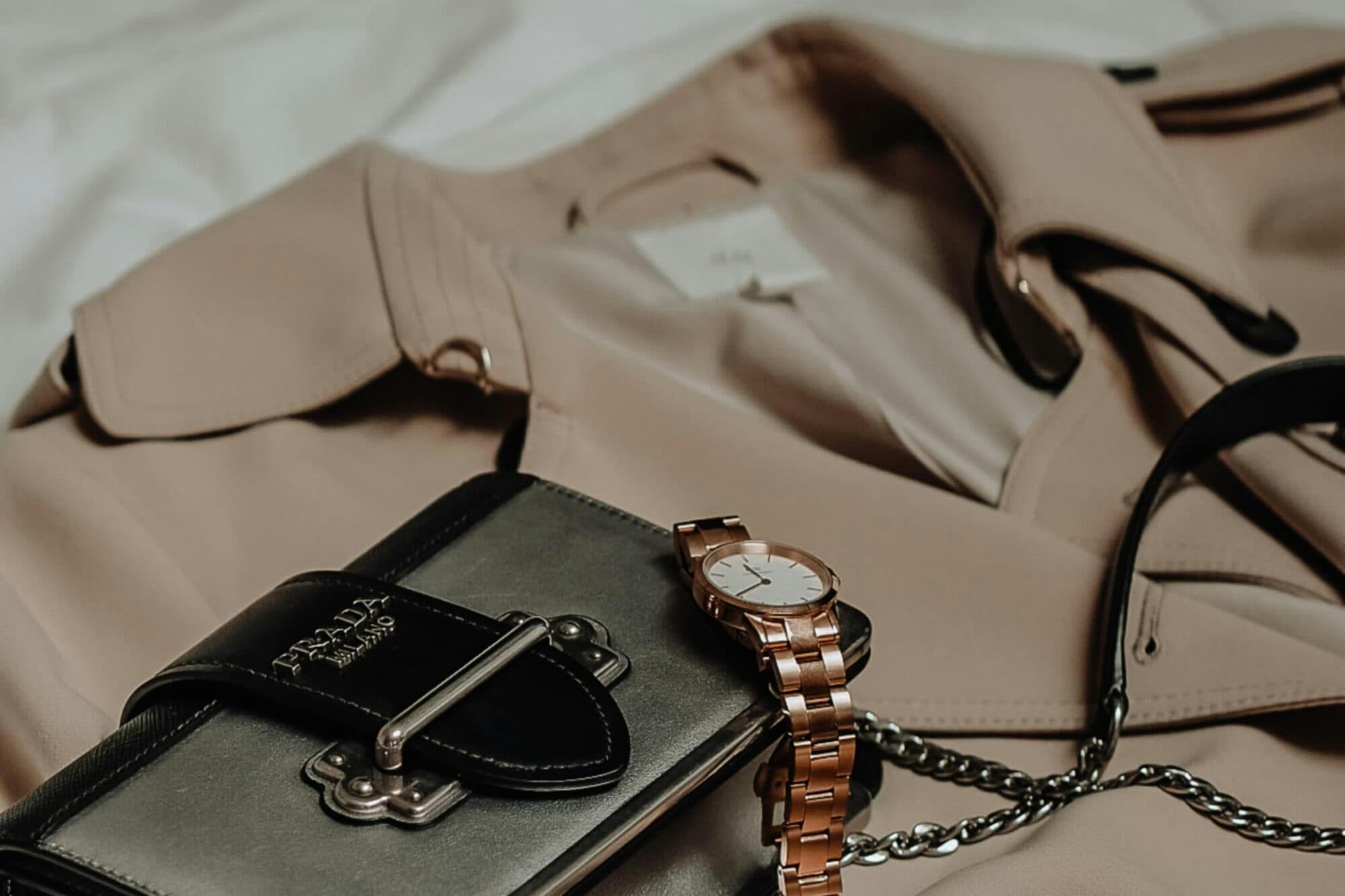 A leather belt, bag charm and pen arranged on a warm neutral ground