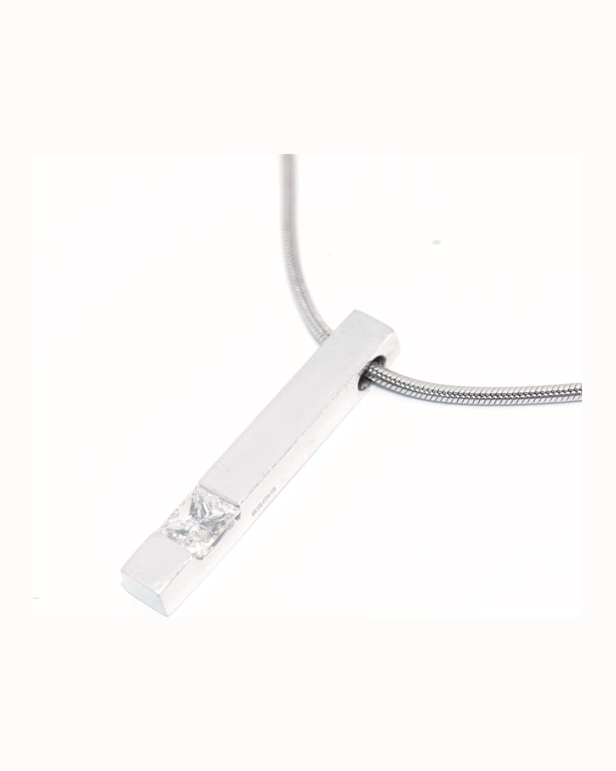 White-gold bar pendant photographed on a neutral ground